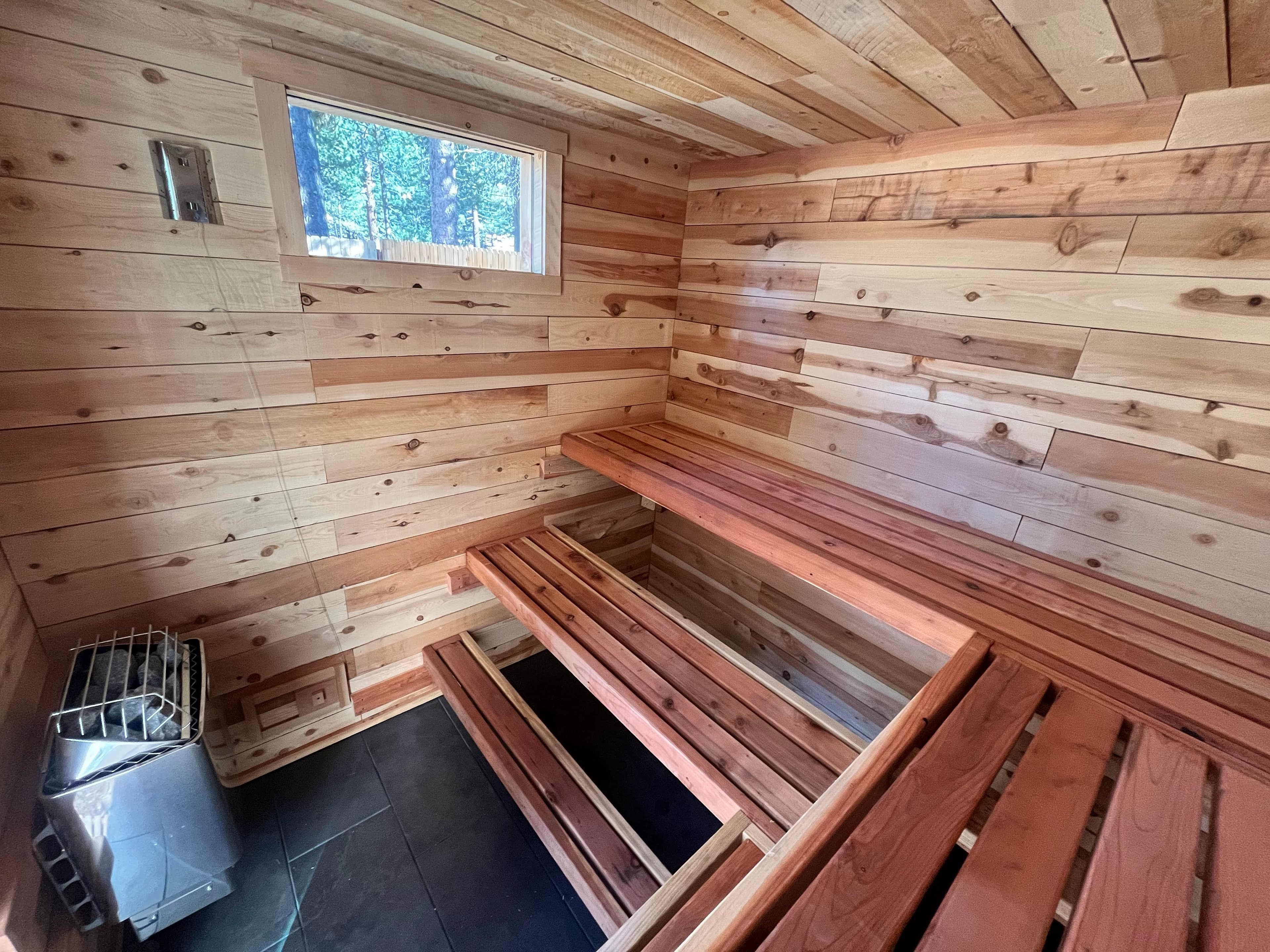 Sauna interior showing cedar paneling, redwood benches with under-bench LED lighting, and two privacy windows