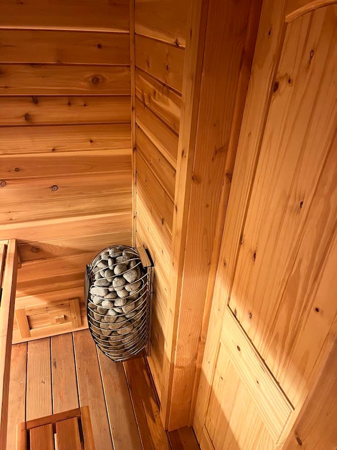 Harvia Spirit 9kW electric sauna heater with rounded stone cage in a cedar-lined corner next to a pine door