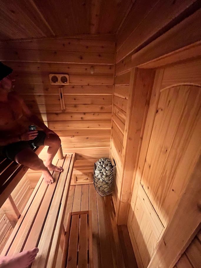 Cedar sauna interior with three-tier L-shaped redwood benches, Harvia Spirit heater, and wall-mounted mechanical ventilation – seats 4-5