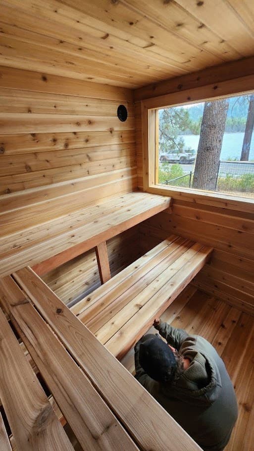 Two-tier cedar benches facing a lake-view window in the Donner Lake deck sauna during the final bench install