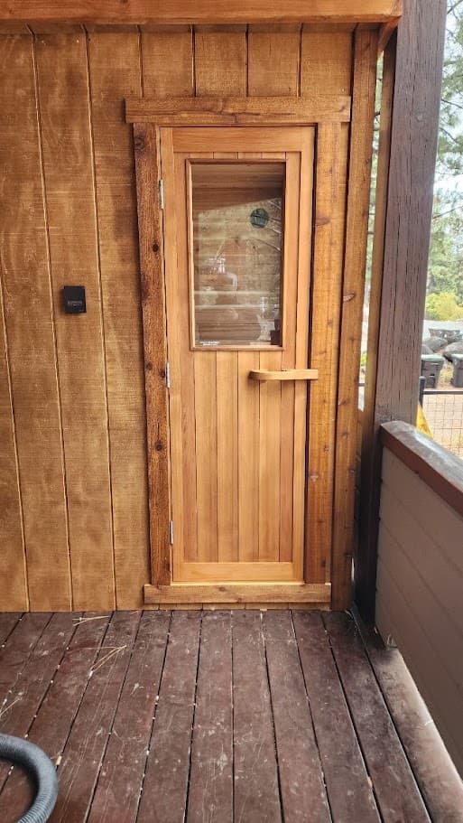 Cedar sauna door with a glass window and an exterior heater control, set on a covered deck near Donner Lake