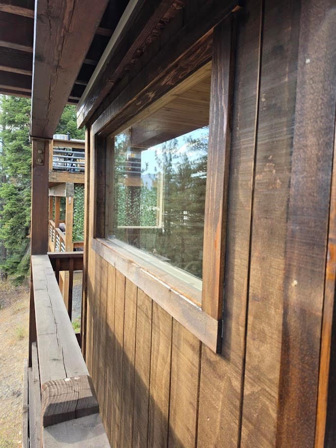 Deck sauna exterior with dark-stained vertical siding and a trimmed picture window, tucked under the upper deck beside the railing