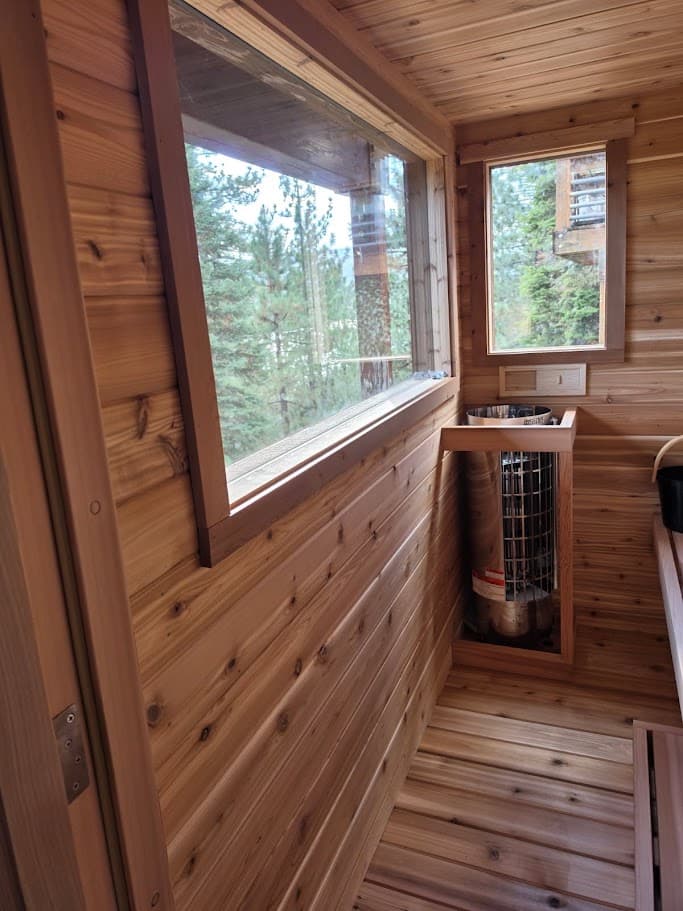 Large picture window and narrow end-wall window looking out at the pines toward Donner Summit from inside the cedar deck sauna