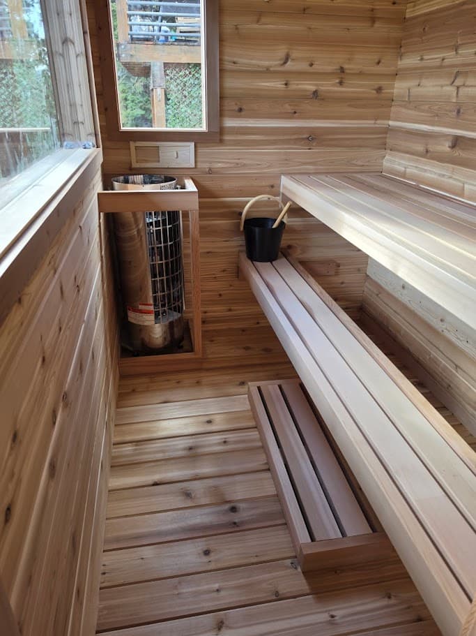 Finished deck sauna interior in Truckee — Harvia Cilindro heater in a cedar surround, long upper bench, lower foot bench, and cedar duckboard floor