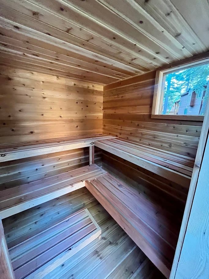 L-shaped multi-tier cedar benches with a window framing the trees and the house beyond – 8x8 hot room in Tahoma