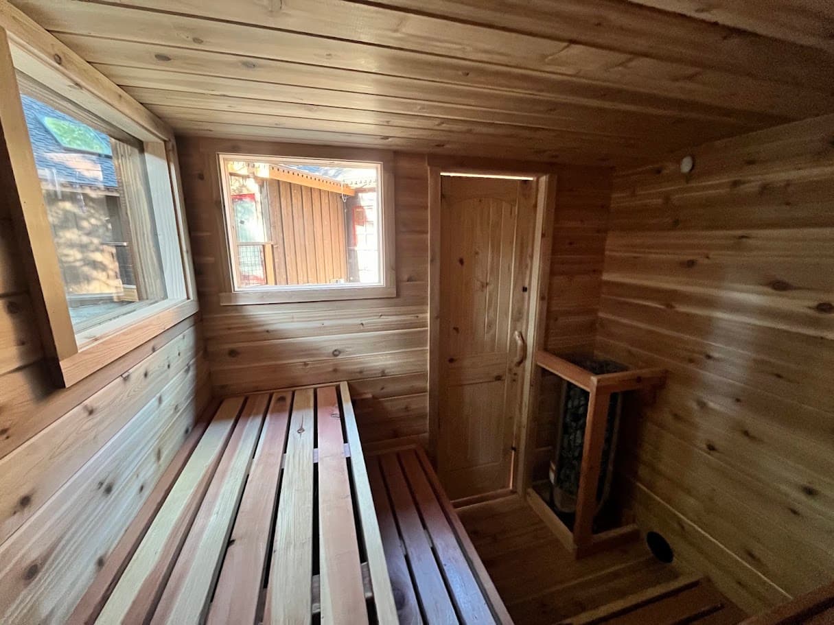 Cedar sauna interior showing the L-shaped bench layout, the corner Harvia Cilindro heater, the solid cedar door, and two view windows