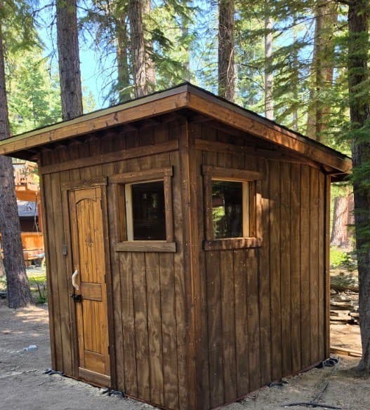 Finished 8x8 outdoor sauna with dark-stained wood siding and a single-slope shed roof, tucked into the pine forest – Tahoma, West Shore Lake Tahoe