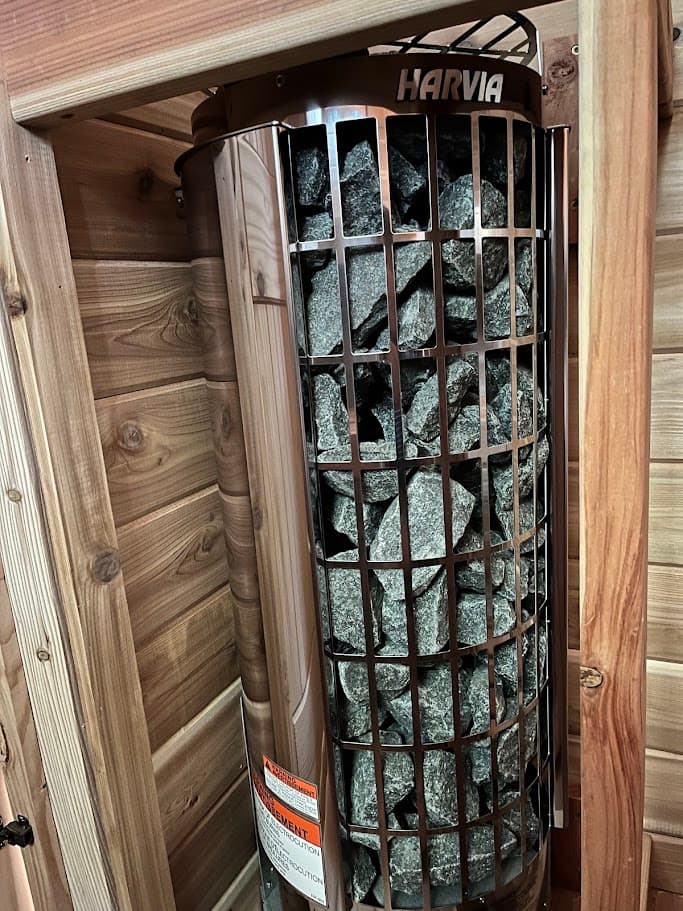 Corner-mounted Harvia Cilindro cylinder heater with a full stone cage, framed in cedar