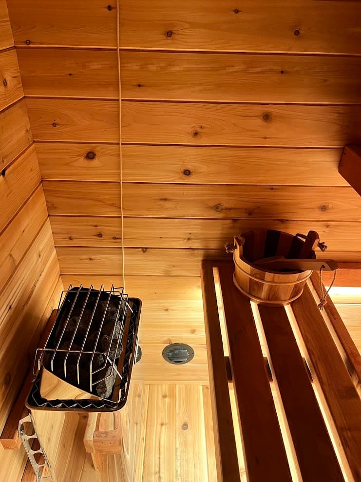 Close-up of Harvia KIP heater with sauna stones, cedar ceiling, and wooden bucket on redwood bench