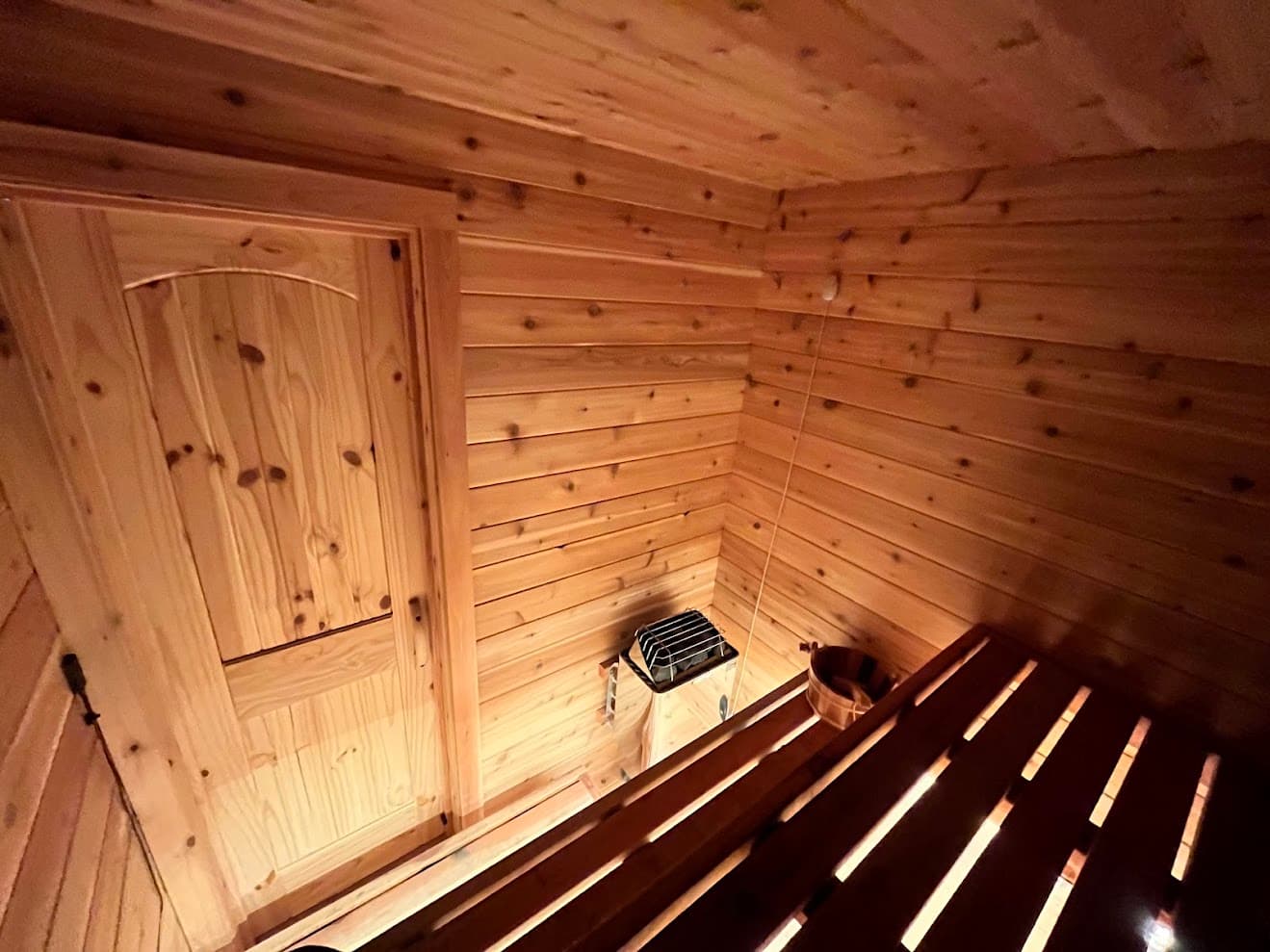 Interior view from top bench looking down at solid wood door, Harvia KIP heater, cedar walls, and under-bench LED lighting