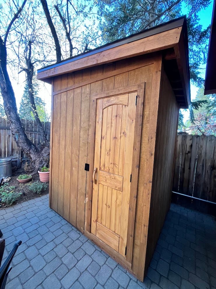 Compact 5x6 outdoor sauna exterior with single-pitch roof, T1-11 siding, and solid wood door on paver patio