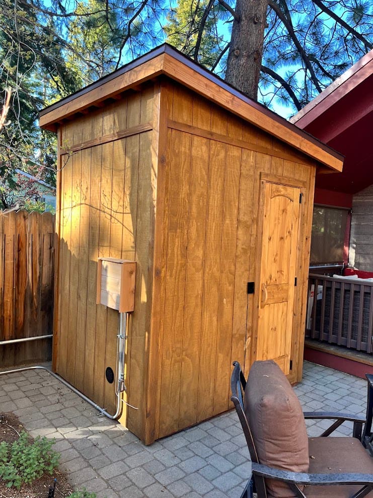 Rear exterior view showing single-pitch roof, electrical conduit, mechanical vent, and stained siding next to house