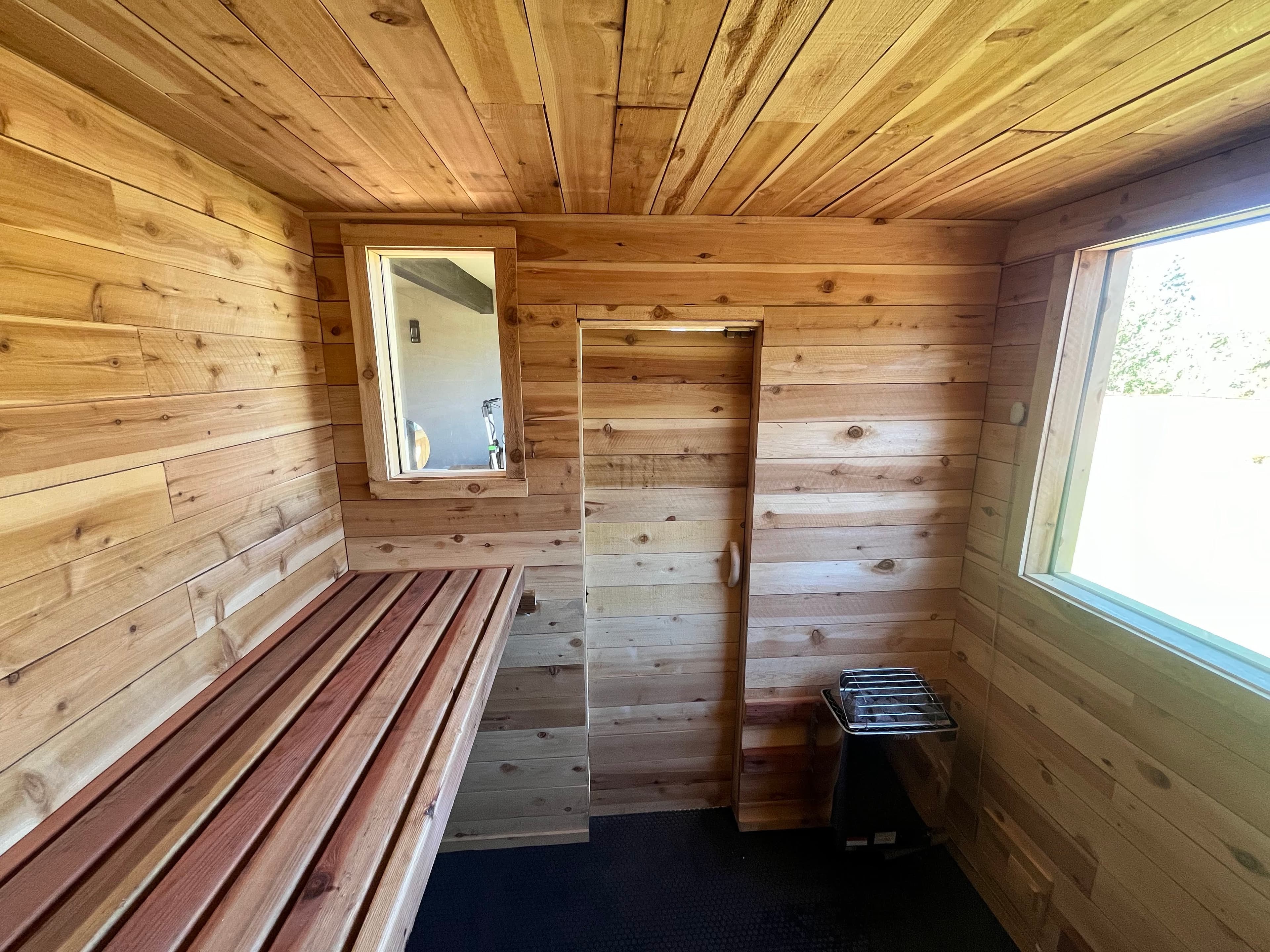Outdoor sauna structure with wood door, gable roof, and deck block foundation