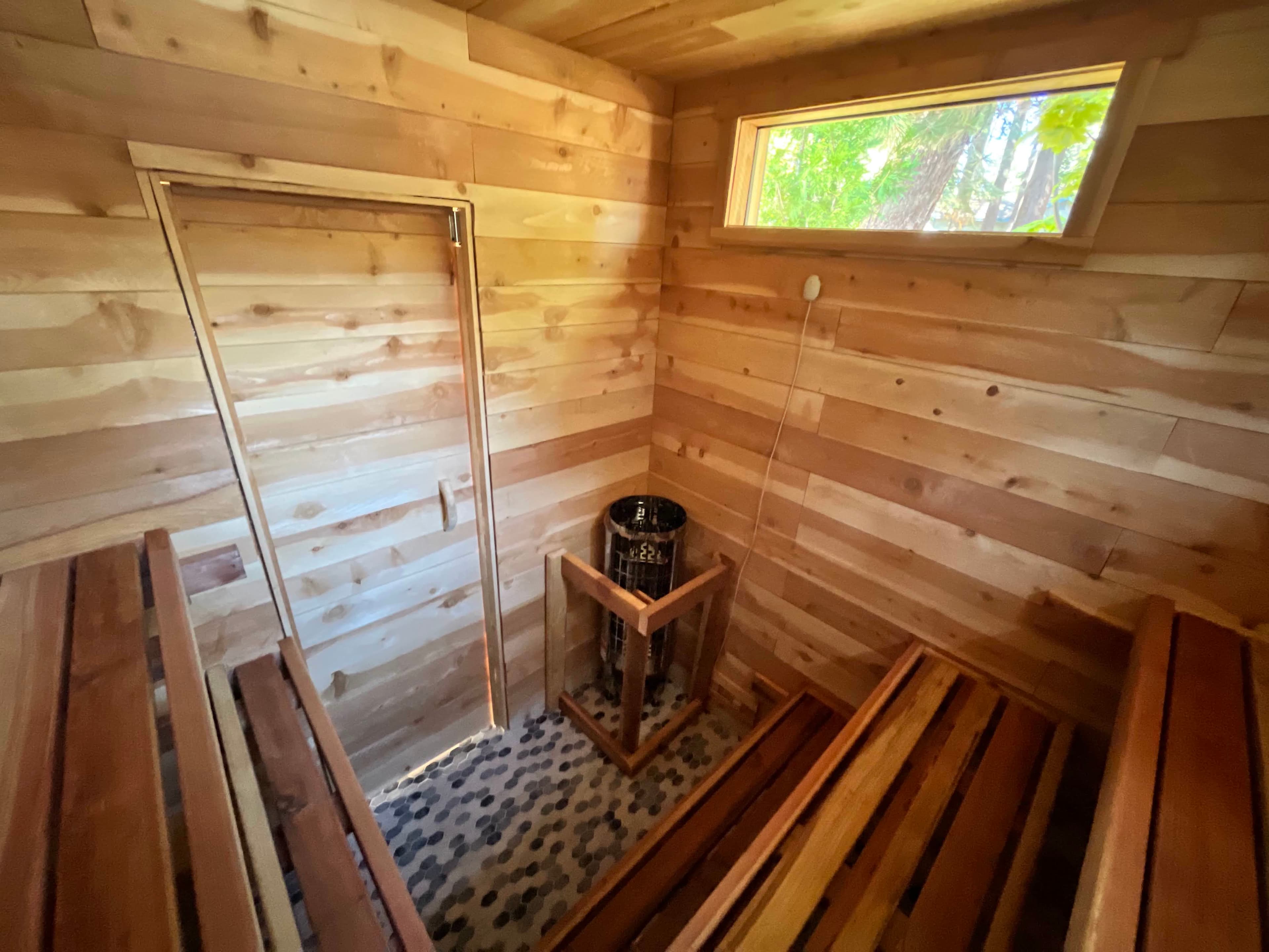 Sauna entry door view showing hex penny tile floor, cedar interior, and two-tier bench layout